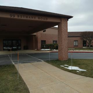 The entrance to a building on a cloudy day, featuring a sidewalk and parking area.