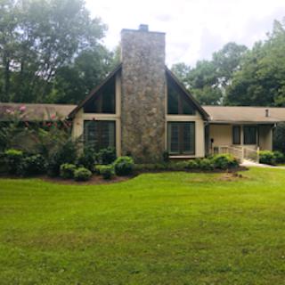 A quaint house with a stone chimney surrounded by lush greenery and a well-maintained lawn.