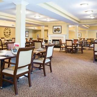 An empty dining room with neatly arranged tables and chairs, carpeted flooring, and warm lighting.