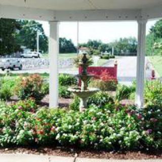 A beautiful garden view from inside a gazebo, featuring a fountain surrounded by lush flowers and greenery.