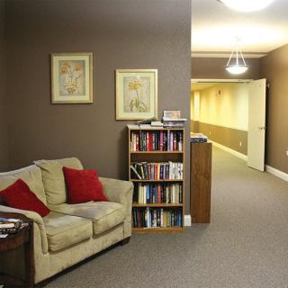 A cozy interior space featuring a sofa with red pillows, a bookshelf, and an adjoining hallway.