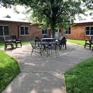 A peaceful courtyard with outdoor seating surrounded by green grass and brick buildings.