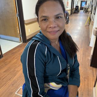 A woman in casual attire smiles while sitting in a healthcare facility.