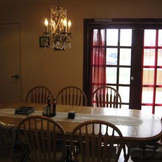 A cozy dining room with a wooden table set for six, illuminated by a chandelier.