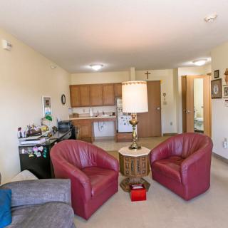 An open-concept living space featuring two red chairs, a small table with a lamp, and a view of the kitchen area.