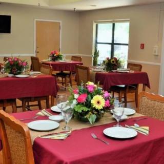 A neatly arranged dining room with tables covered in red tablecloths, set with plates and glasses, and adorned with floral centerpieces.