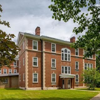 A historic brick building surrounded by trees under a cloudy sky.