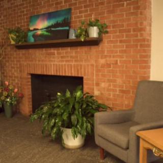 Cozy living room with a brick fireplace, adorned with indoor plants and artwork.