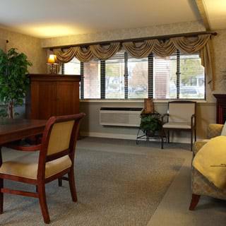 A cozy living room with a large window, traditional furniture, and decorative plants.