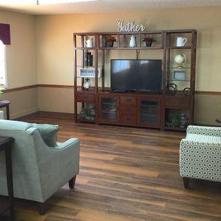 A cozy living room with a TV and comfortable seating arrangement, featuring wood flooring and decorative shelves.