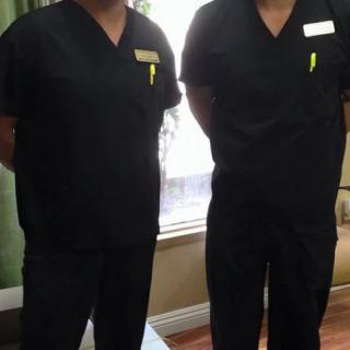 Two individuals wearing black scrubs stand indoors, suggesting a healthcare setting.