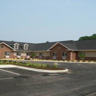 A single-story brick building with a dark roof, adjacent to an empty parking lot.
