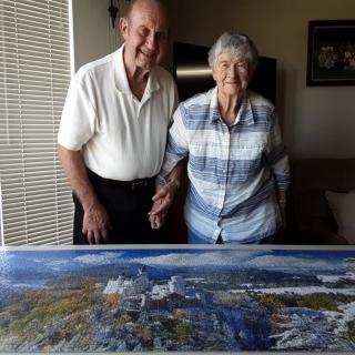 An elderly couple smiling and posing with a painting indoors.