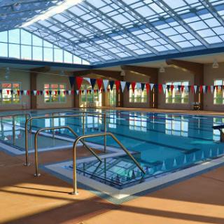 A bright and spacious indoor swimming pool featuring large windows and decorative flags.