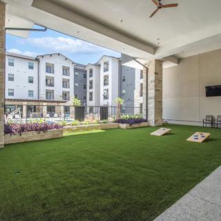 A modern apartment complex featuring an open recreational area with a well-maintained lawn and cornhole games.