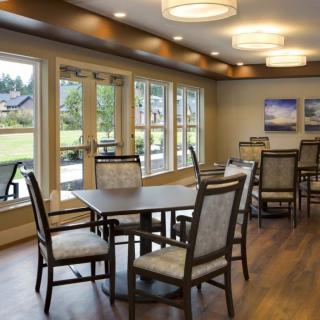 A well-lit dining room with wooden flooring and large windows overlooking a garden.