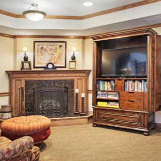 A cozy living room with a fireplace and a television set on a wooden bookshelf.