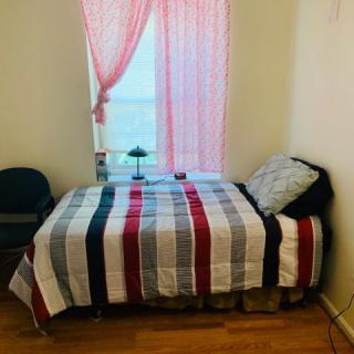 A cozy bedroom with a neatly made bed featuring a striped blanket, next to a window with pink curtains.