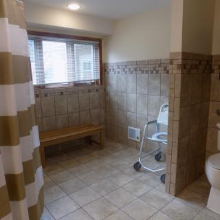 An accessible bathroom featuring tiled walls, a shower with a curtain, and a shower chair.