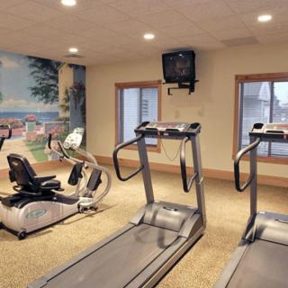 A gym with two treadmills and a stationary bike, featuring large windows and a wall-mounted TV.