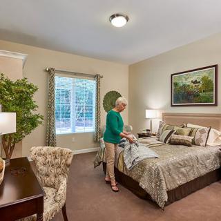 A woman making the bed in a well-decorated bedroom with various furniture and decor elements.