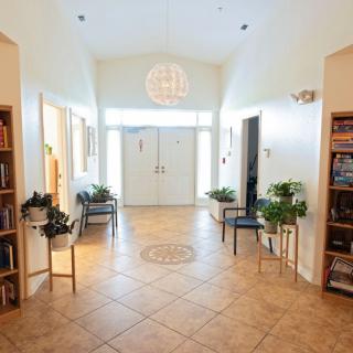 A bright hallway with tile flooring, plants, bookshelves, and chairs leading to a set of double doors.