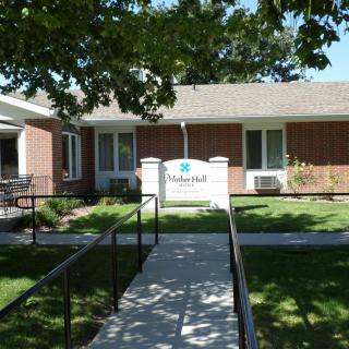 A one-story brick building with a sign in front, surrounded by trees and featuring a paved walkway leading to the entrance.