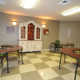 A spacious interior room featuring tables and chairs with a decorative cabinet in the background.