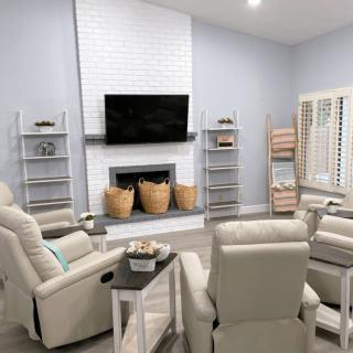 A modern living room featuring a central fireplace with a mounted TV, surrounded by comfortable armchairs and decorative shelving.