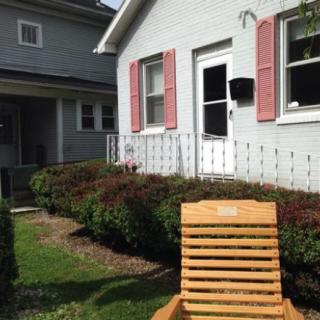 A quaint house with pink window shutters and a wooden chair in the front yard.