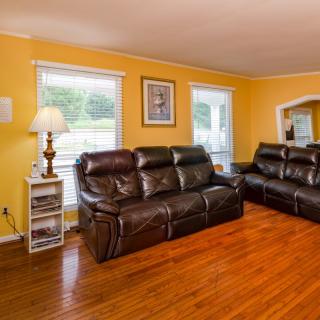 A cozy living room with yellow walls, featuring two leather sofas, wooden flooring, and ample natural light from the windows.