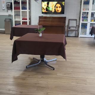 A dining area featuring a brown table with a plant, set against a backdrop of hardwood flooring and a television.