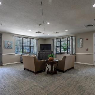 A cozy living room with two armchairs facing a television, surrounded by large windows.