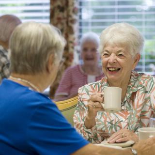 Elderly women enjoying a conversation over coffee in a communal setting.