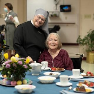 A joyful moment shared between a caregiver and an elderly resident in a nursing home, surrounded by a pleasant dining setup.