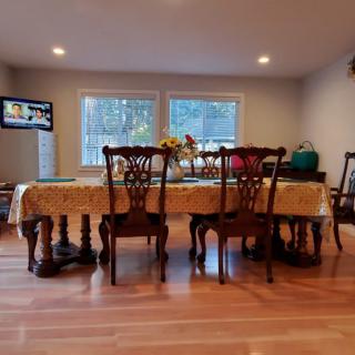 A cozy dining room with a wooden table set for meals, featuring elegant chairs and a television on the wall.