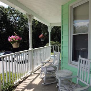 A charming porch decorated with hanging flowers and inviting rocking chairs, perfect for a relaxing day.