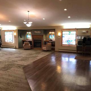 A spacious living room with a mix of carpet and hardwood flooring, featuring comfortable seating, large windows, and a fireplace.