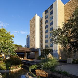 A view of a modern hotel building surrounded by landscaped greenery under a clear sky.