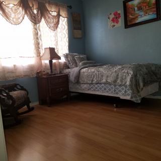 A cozy bedroom with a single bed, a nightstand with a lamp, and a rocking chair by the window.