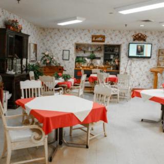 An empty dining area with tables covered in red tablecloths and surrounded by wooden chairs.