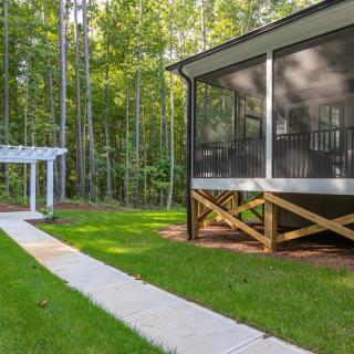 A serene backyard featuring a screened porch, pergola, and a pathway leading into lush greenery.