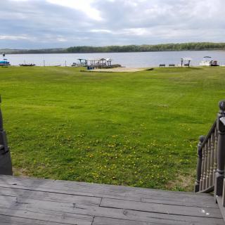 A scenic view of a grassy area leading to a lake with boats, under a cloudy sky.
