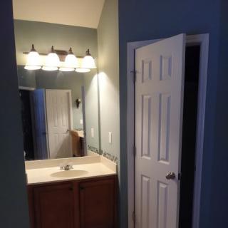 A bathroom with a large mirror, sink, and bright overhead lighting beside an open door.