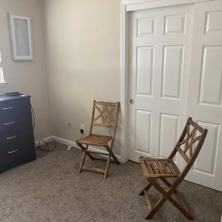 A minimalist room with two wooden chairs, a dresser, and a closet.