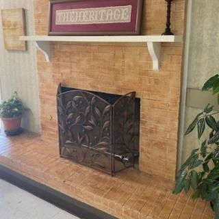 A cozy fireplace with an ornate metal screen and decorative shelf above.