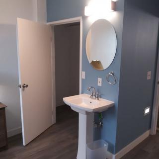 A bathroom with a pedestal sink, circular mirror, and blue walls.