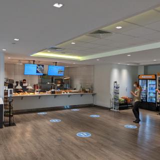 A spacious and modern cafe interior featuring a coffee bar, seating area, and multiple screens.