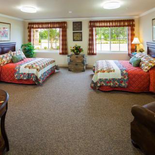 A cozy bedroom with two beds, colorful decor, and large windows.