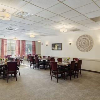 A spacious dining room with arranged tables and chairs, featuring soft lighting and decorative elements.